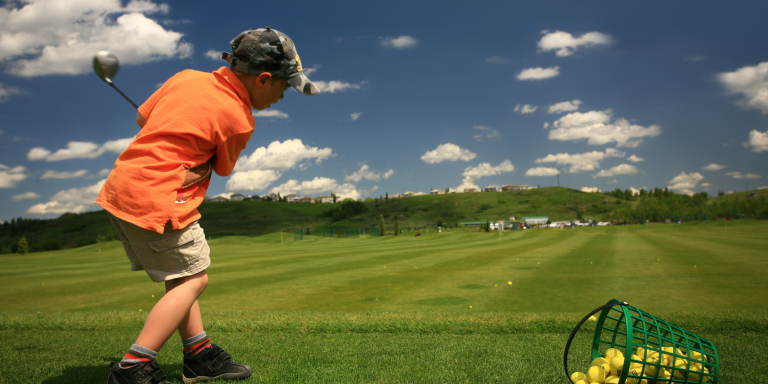 Image of boy in orange polo shirt swinging a golf club